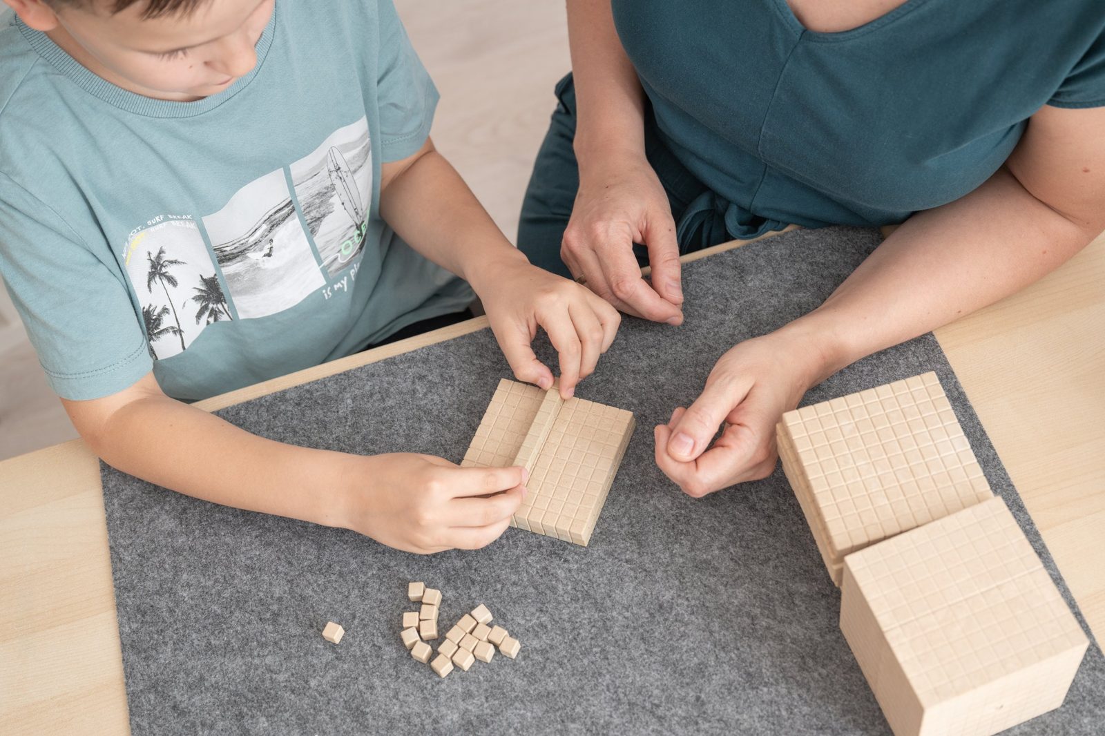Kinderhände legen Hunderterplatten und Zehnerstangen aus Holz